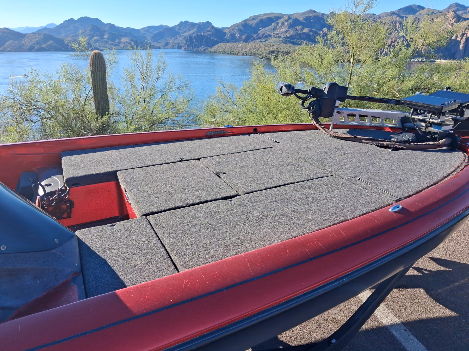 Bow deck of a red bass boat with fresh gray carpet, parked above Saguaro Lake with saguaro cactus and desert mountains behind