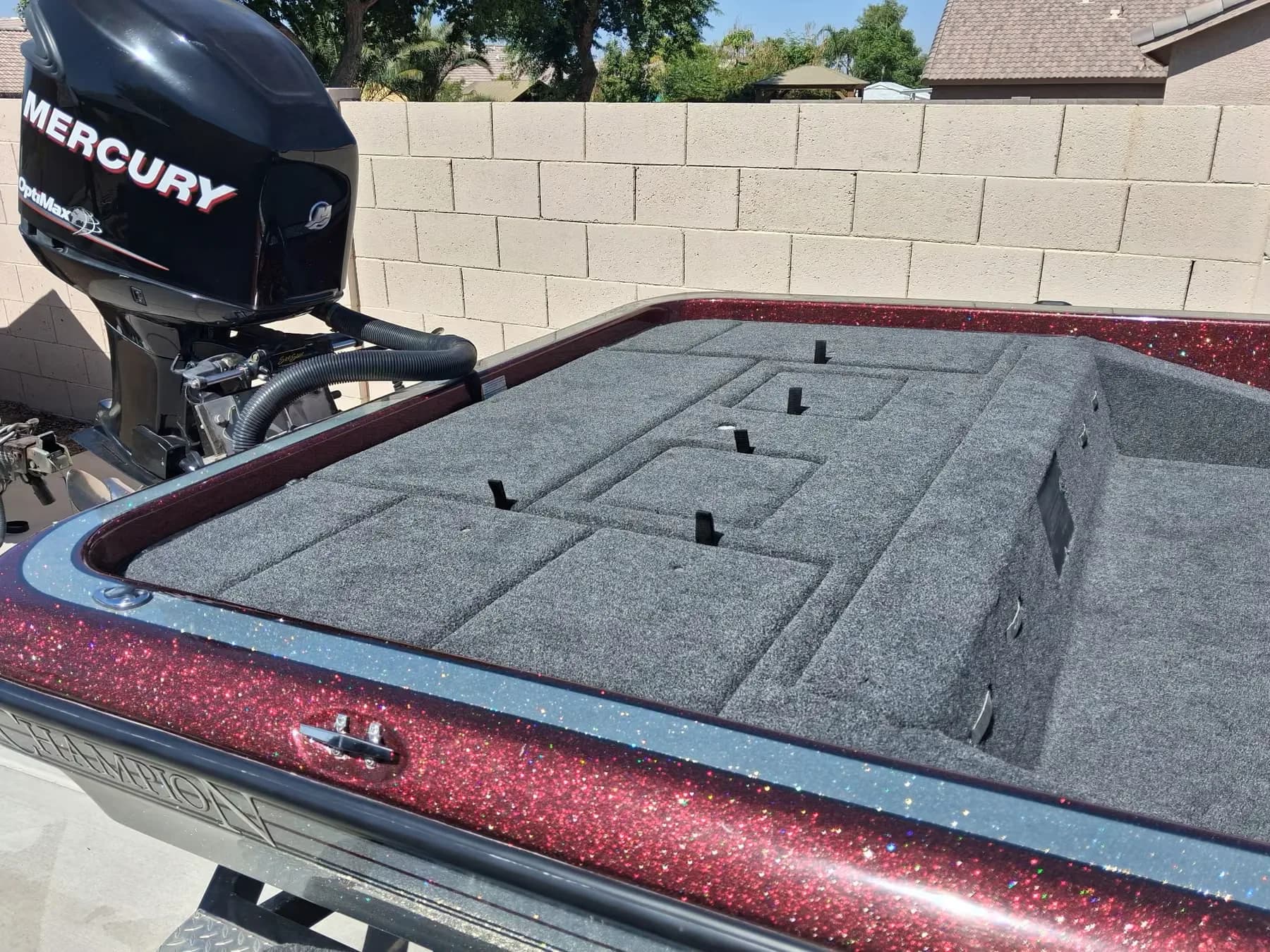 Rear deck of a burgundy metalflake Champion bass boat with newly installed gray marine carpet, rod straps and hatch lids cut in