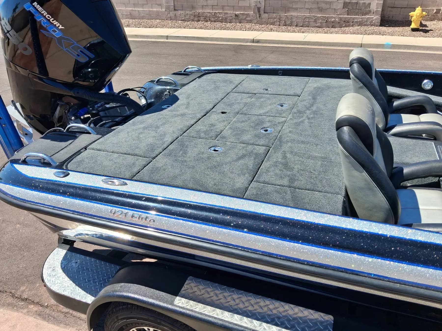 Rear deck and seats of a blue metalflake bass boat with fresh gray carpet, behind a Mercury Pro XS outboard
