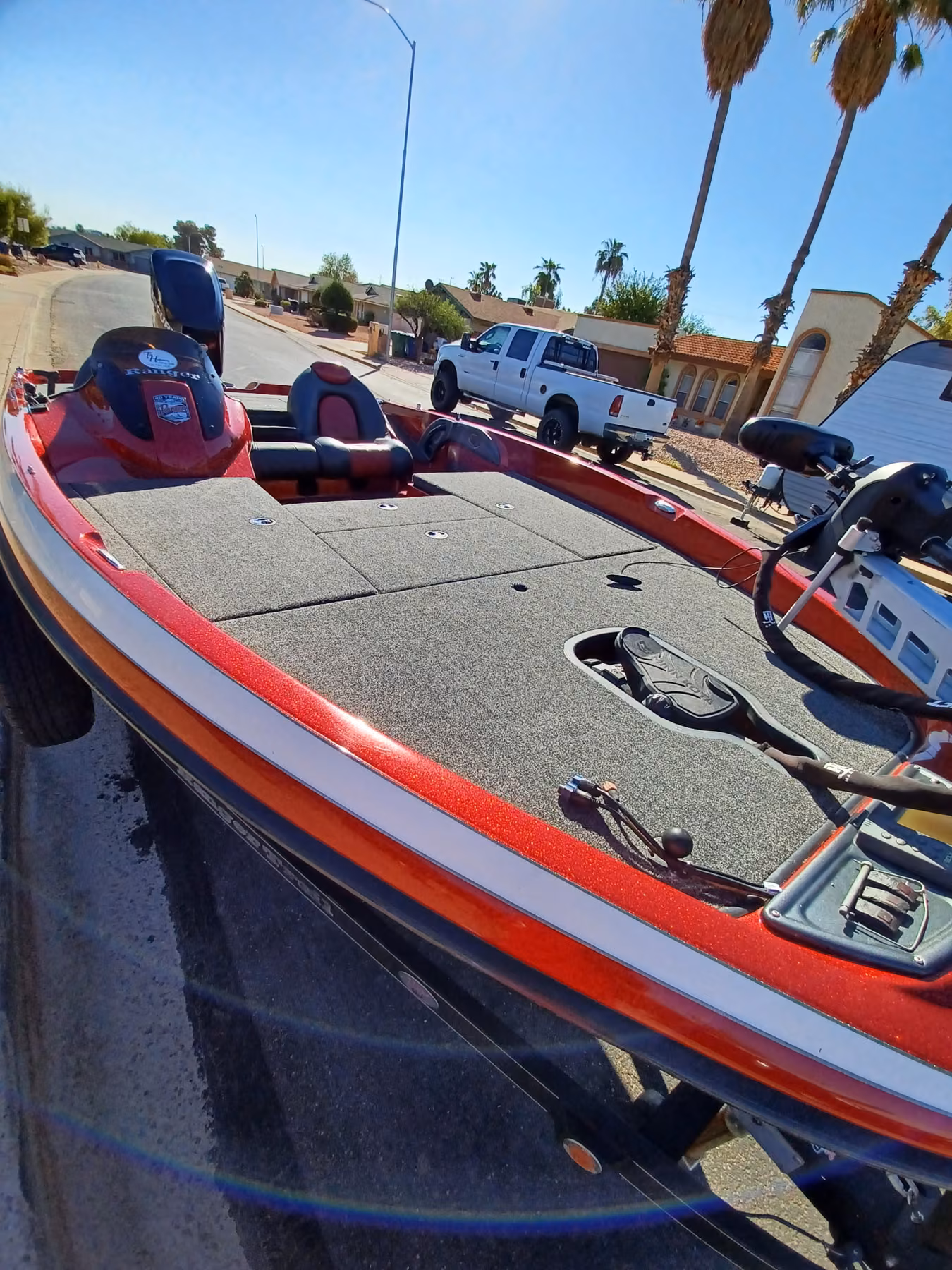 Red Ranger bass boat on its trailer at the curb, deck and gunwales visible along the full length of the hull